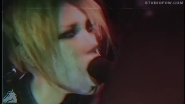 A close-up shot of a woman with blonde hair and heavy eyeliner singing into a microphone in a dark setting. Screenshot from Agent Of Chaos