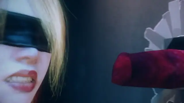 A blonde woman with a black blindfold over her eyes and a shocked expression looks towards a large, erect penis entering her from the right side of the frame. Screenshot from Scarlet Nights