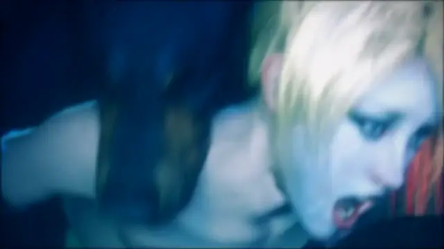 A close-up shot shows a girl with blonde hair and wide blue eyes expressing a look of shock or ecstasy while being intimate with another person in a dark setting. Screenshot from Scarlet Nights
