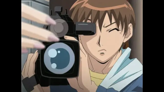 A brown-haired anime man with one eye closed holds a professional video camera, filming a woman with long, manicured fingernails reaching into the frame. Screenshot from Foxy Nudes - Episode 2