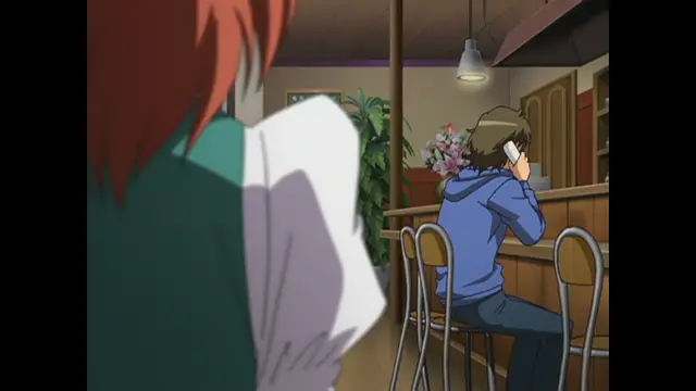 A girl with red hair and a white shirt stands in the foreground looking toward a man in a blue hoodie who is sitting at a bar counter and talking on a cellphone. Screenshot from Cafe Junkie - Episode 1
