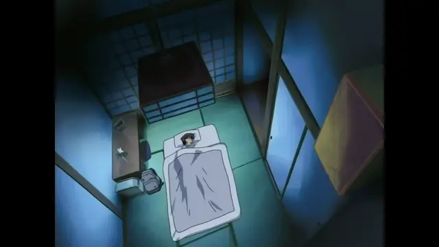 A man with black hair lies in a bed in a dimly lit Japanese-style room, covered by a grey blanket. Screenshot from Slave Nurses - Episode 1