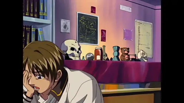 A male anime character with light brown hair and a shocked expression sits at a desk in a room filled with various decorations and shelves, including a skull and various figurines. Screenshot from Discipline - Episode 2