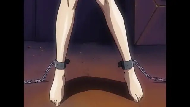 A woman's legs and feet are shown from the knees down as she stands with her ankles bound by heavy metal shackles and chains in a dark room. Screenshot from Discipline - Episode 3