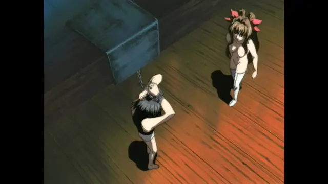 A bald man with a black beard is chained to a post in a room, looking up at a small-breasted girl with pink hair ribbons who is approaching him. Screenshot from Guren - Crimson Lotus - Episode 2