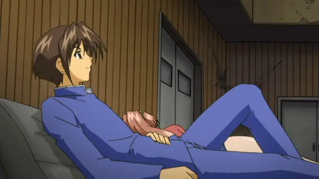 A boy in a blue school uniform lies on a bed while a girl with pink hair rests her head on his lap, looking up at him in a room with wood-paneled walls. Screenshot from Grope: Yami no naka no Kotoritachi - Episode 1