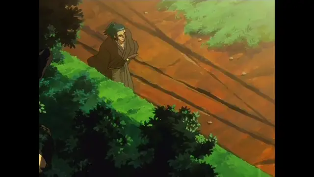 An older man with graying hair and a beard, wearing a traditional brown kimono, walks along a dirt path surrounded by lush green bushes and trees. Screenshot from The Last Kunoichi - Episode 2