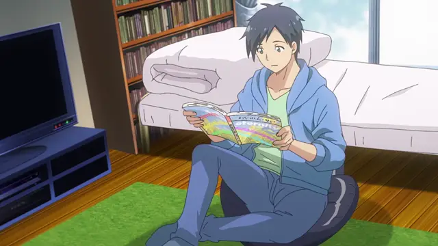A young man with dark hair sits on a blue beanbag chair in a living room, looking surprised as he reads a colorful magazine that says "ファンタジー" (Fantasy) on the cover. Screenshot from Kimi ga Suki - Episode 1