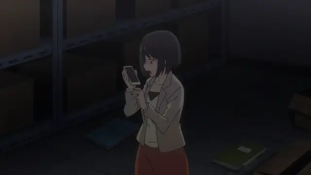 A shocked-looking woman with short black hair stands in a dark storage room, holding a smartphone in both hands. Screenshot from Eternity: Shin`ya no Nurekoi Channel - Episode 9
