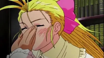 A blushing blonde girl with a pink bow and ruffled collar covers her face with her hand while standing in front of a library bookshelf. Screenshot from Hinadori no Saezuri - Episode 1